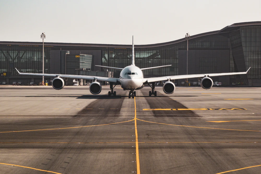 An unmarked wide-body airliner taxiing past a terminal building